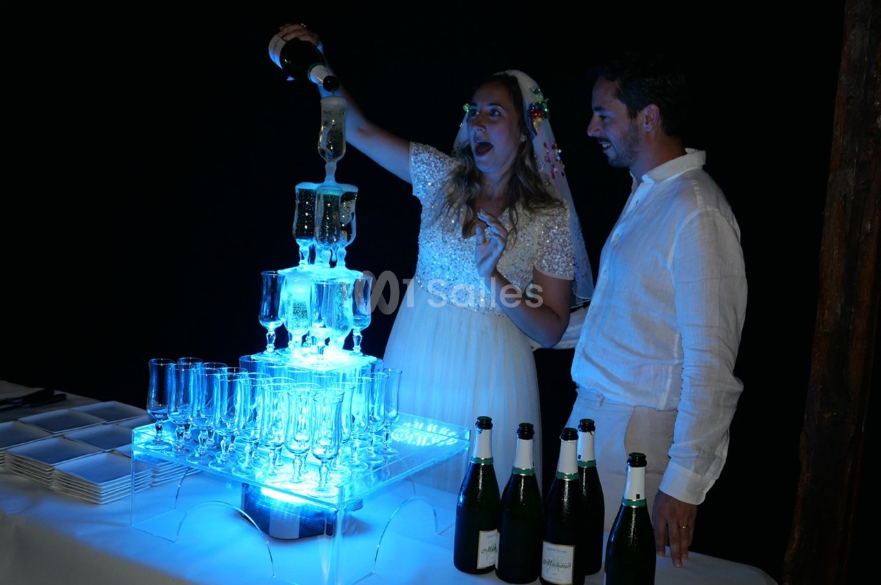 Une femme verse du champagne dans une fontaine lumineuse en verre, accompagnée d'un homme, dans un cadre festif.