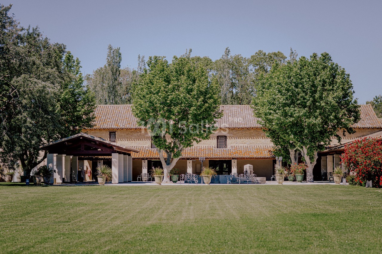 Grande maison en pierre entourée de verdure, avec une pelouse bien entretenue et des arbres imposants.