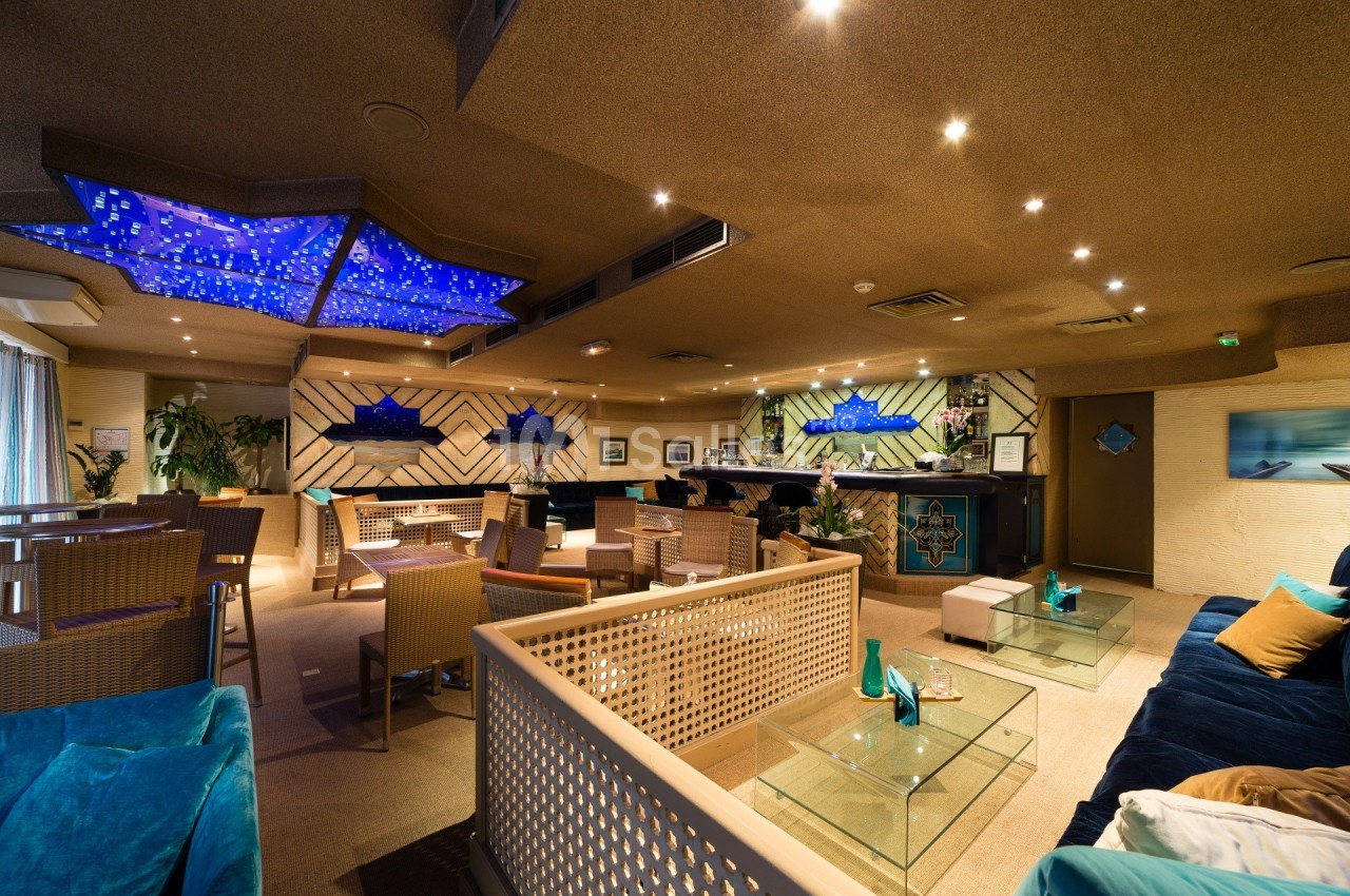 Salle de restaurant moderne avec éclairage bleu au plafond, mobilier en rotin et décoration contemporaine.