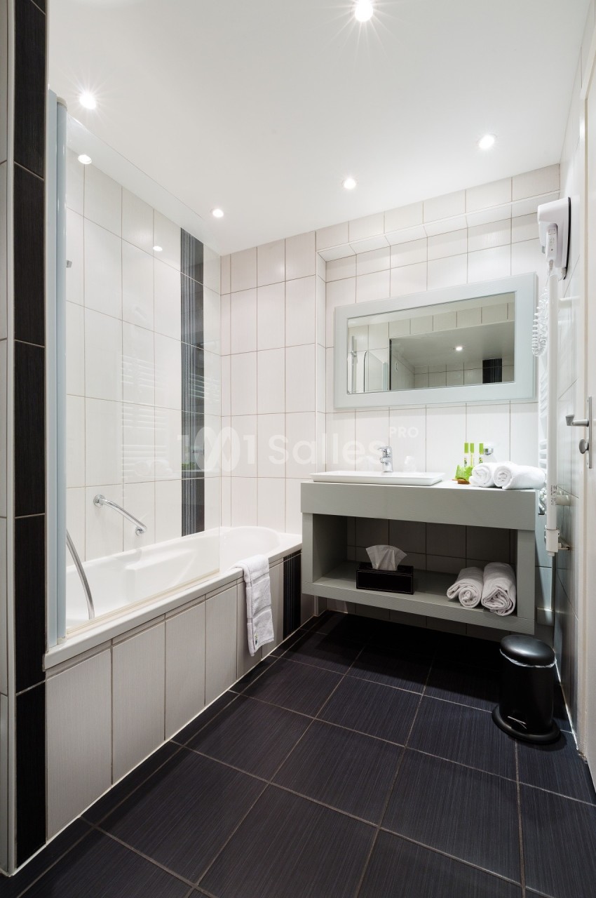 Salle de bain moderne avec baignoire, lavabo, miroir, carrelage noir et blanc, et éclairage encastré.