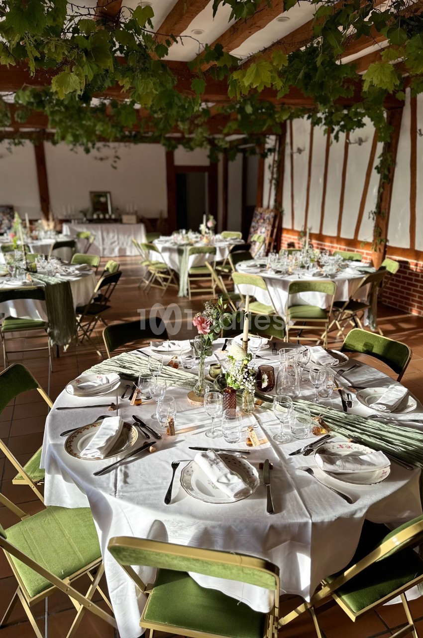Salle de réception décorée avec des tables rondes dressées, nappes blanches et chaises vertes, sous un plafond orné de…