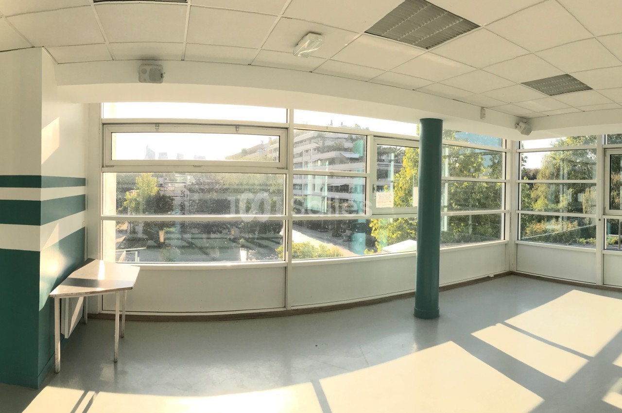 Vue panoramique d'une salle lumineuse avec de grandes fenêtres donnant sur un espace extérieur arboré.