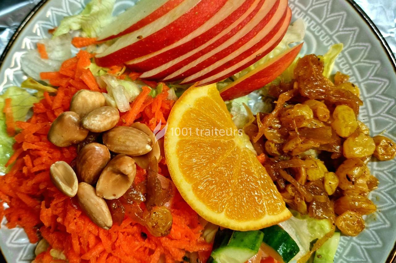 Assiette composée de salade, carottes râpées, amandes, pommes en tranches, raisins secs et une rondelle d'orange.