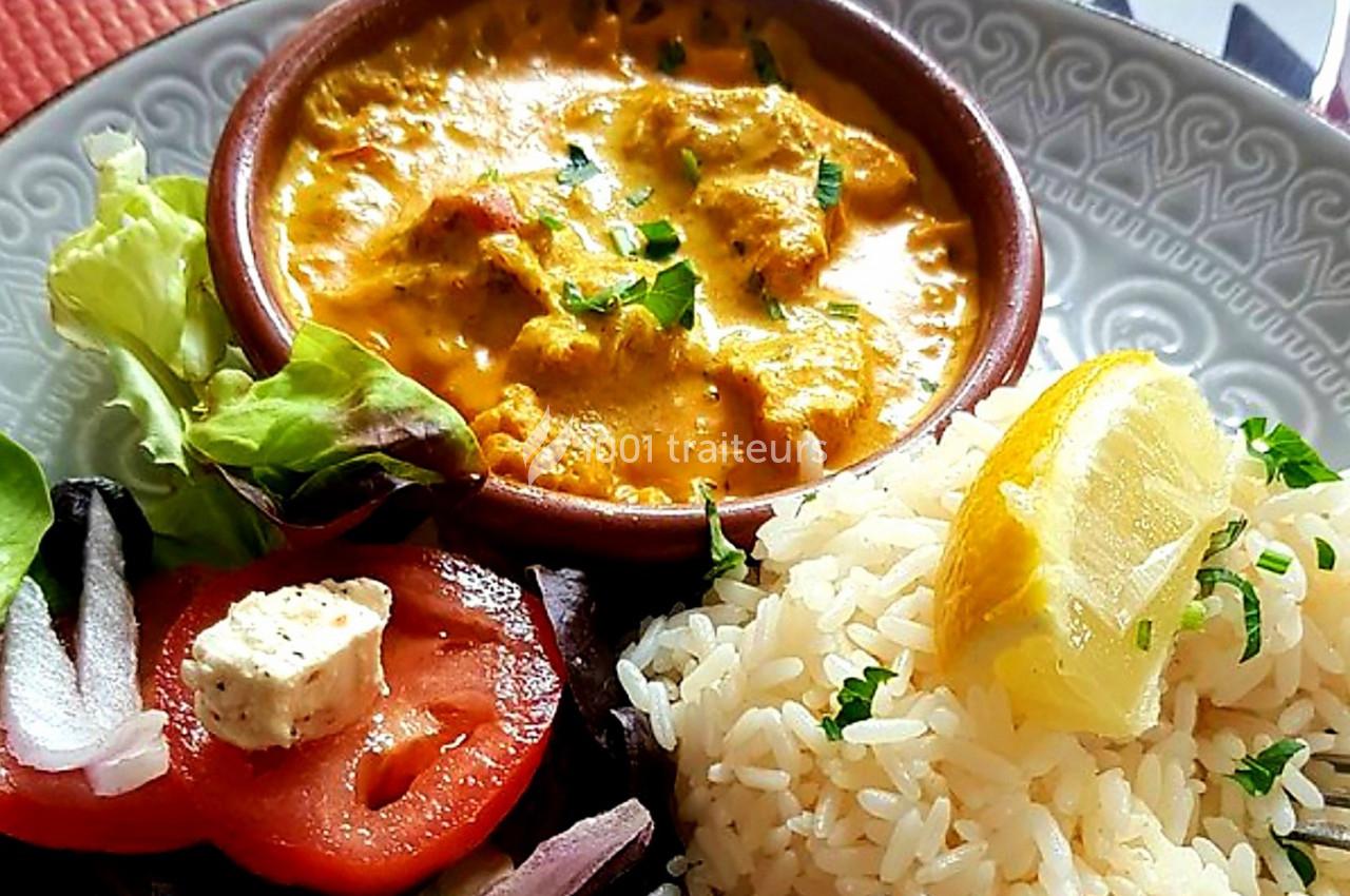 Plat composé de poulet au curry dans un bol, accompagné de riz, salade verte et rondelles de tomate.