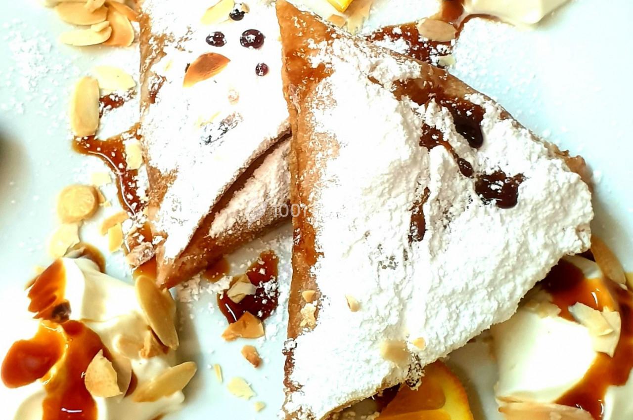 Triangles de pâte croustillante saupoudrés de sucre glace, accompagnés de crème, amandes et sauce caramel.