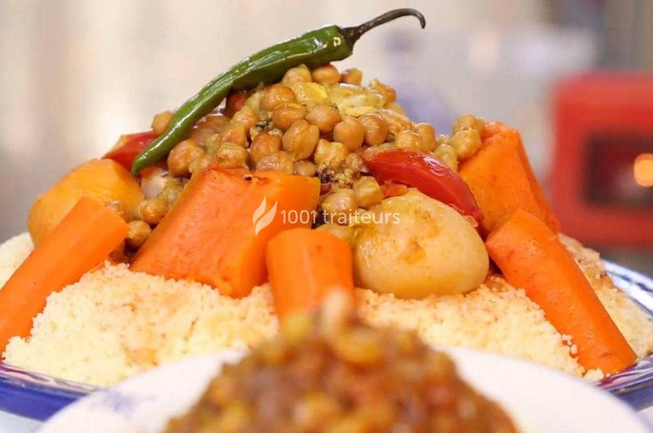 Assiette de couscous garnie de légumes variés, pois chiches et piment vert, présentée sur un plat blanc.