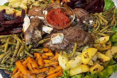 Assiette garnie de légumes variés, morceaux de viande et sauce rouge au centre, présentée sur un lit de salade.