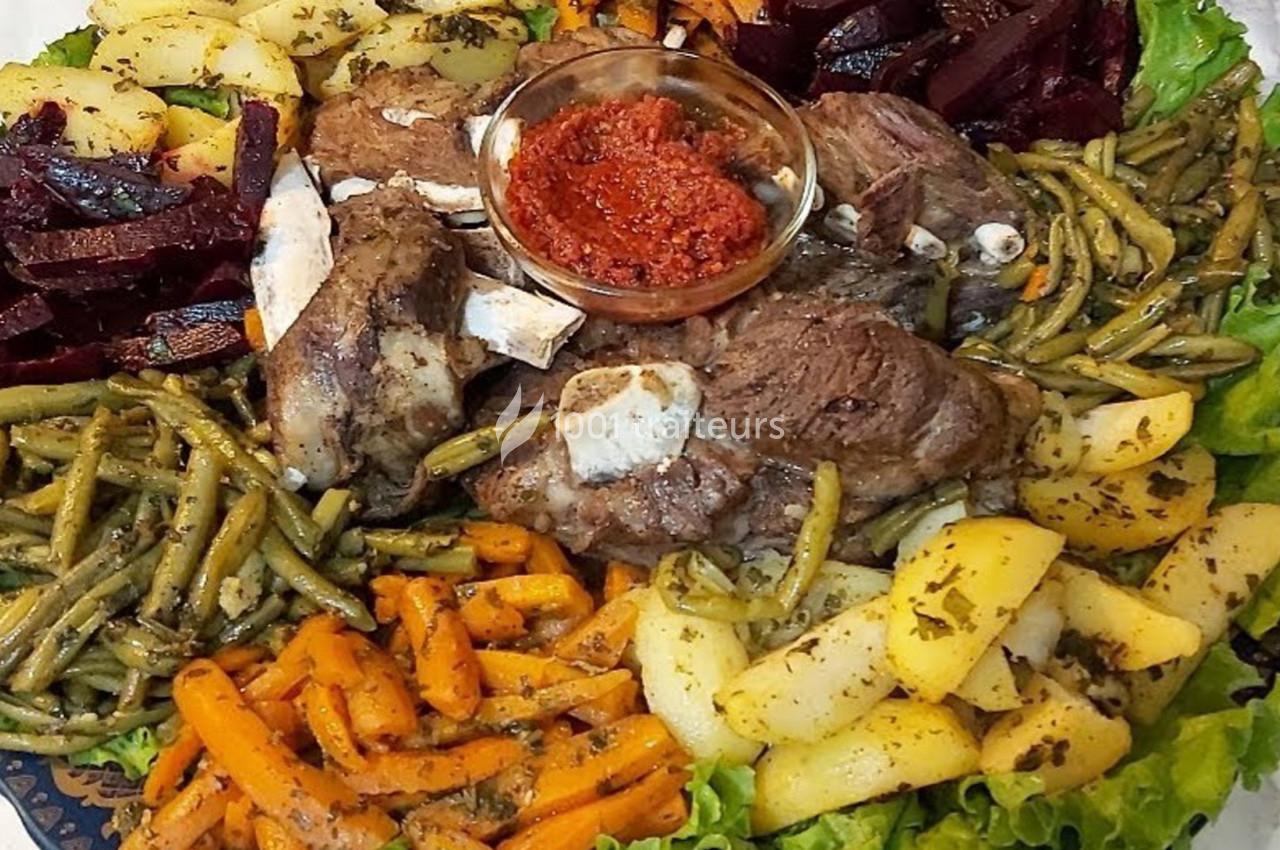 Assiette garnie de légumes variés, morceaux de viande et sauce rouge au centre, présentée sur un lit de salade.
