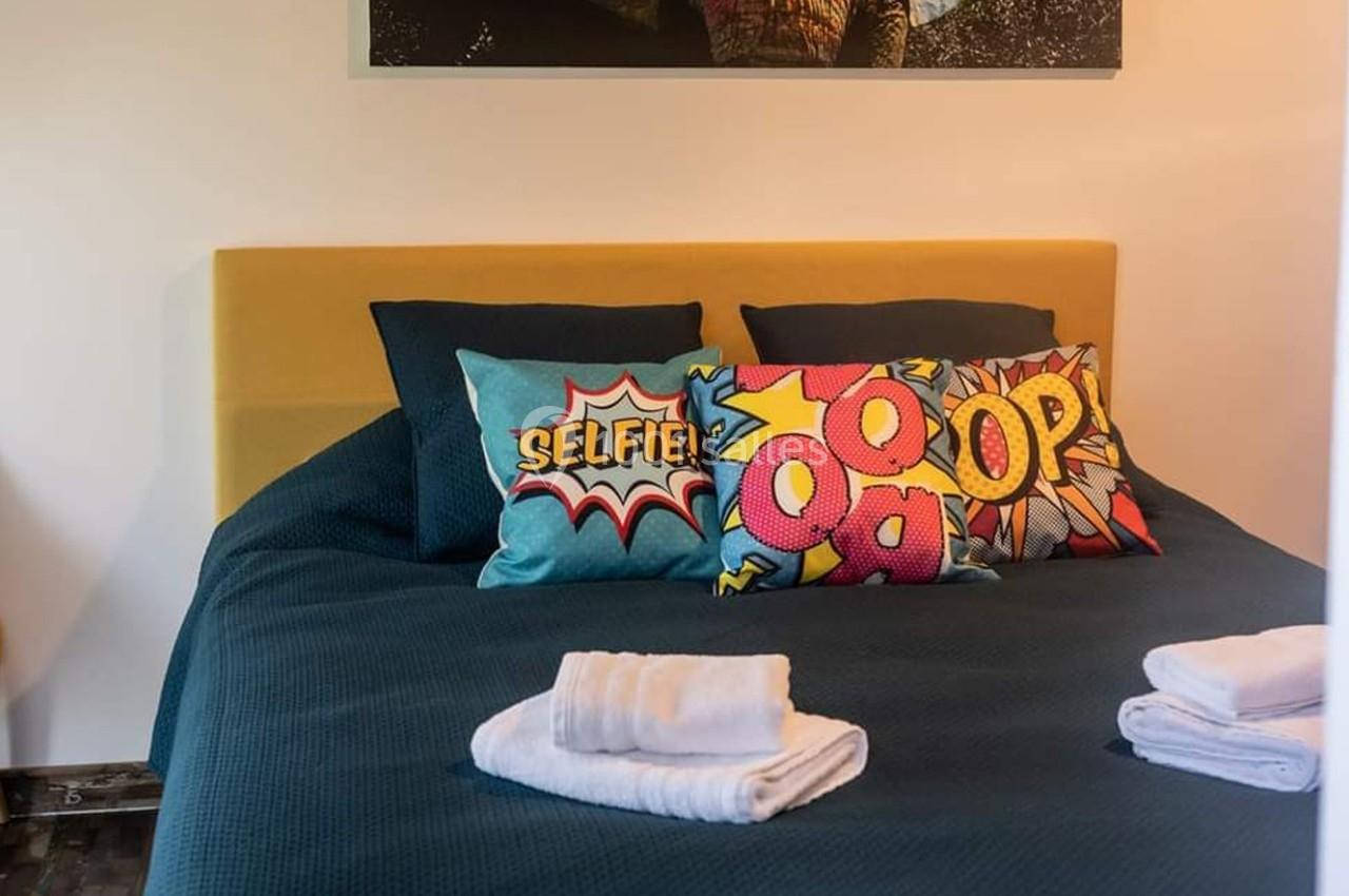 Lit avec tête de lit jaune, coussins colorés à motifs de bande dessinée et serviettes pliées au premier plan.