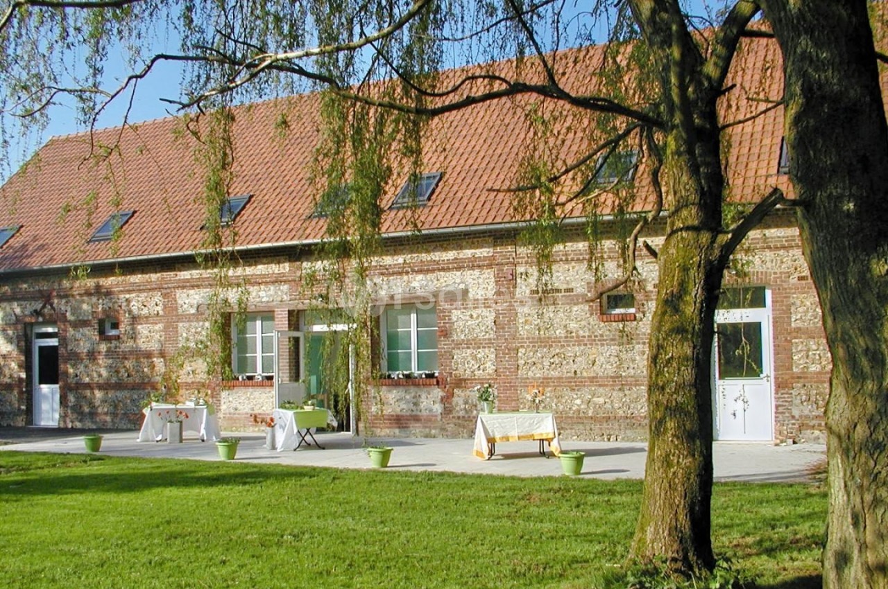 Bâtiment en briques avec toit en tuiles rouges, entouré d'arbres et d'une pelouse, tables dressées à l'extérieur.