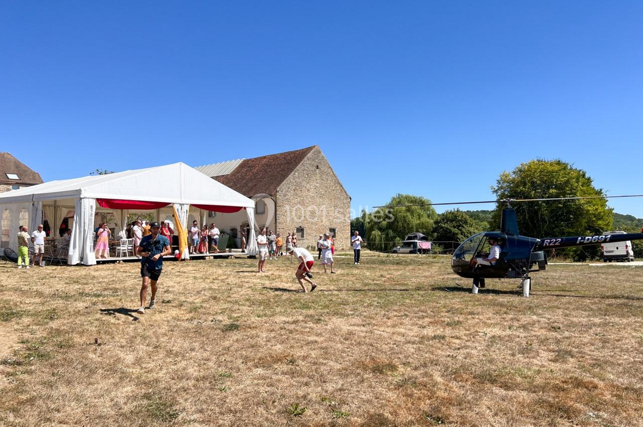 Un hélicoptère posé sur un terrain herbeux près d'une tente blanche où des personnes sont rassemblées.