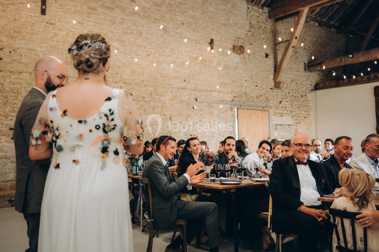 Un couple face à des invités assis dans une salle en pierre décorée de guirlandes lumineuses.