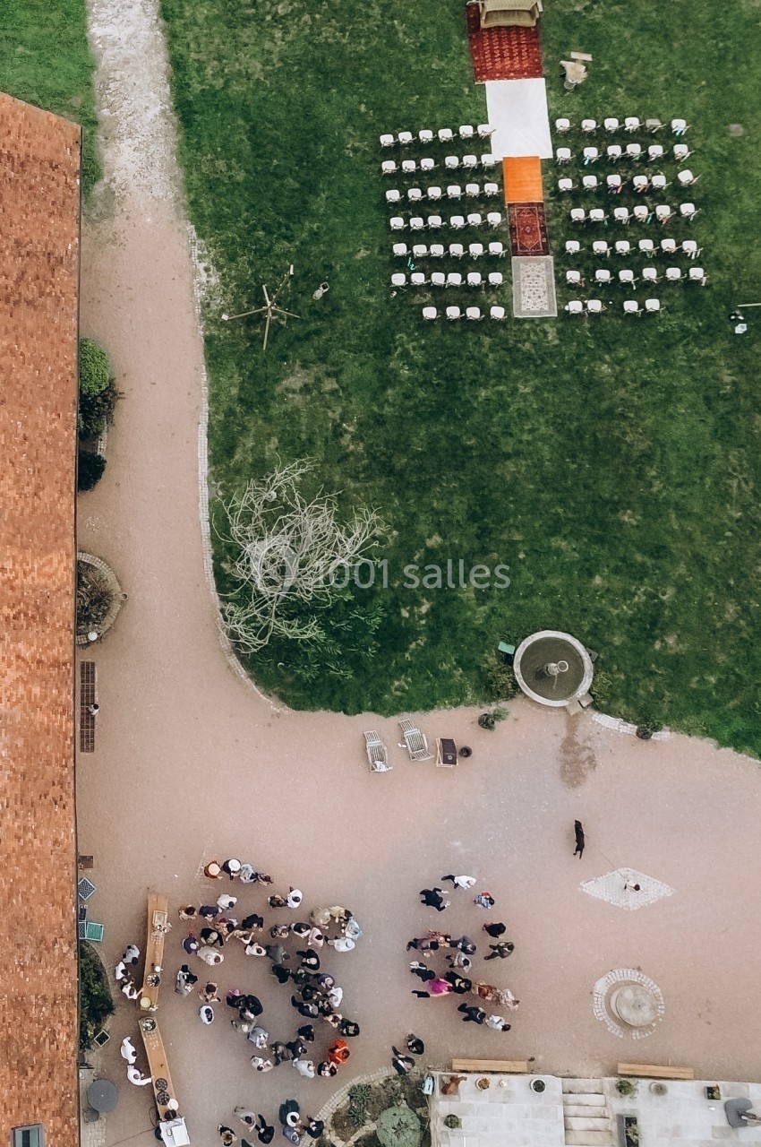 Vue aérienne d'une cérémonie en plein air avec des chaises alignées, un tapis rouge et des invités rassemblés près d'un…
