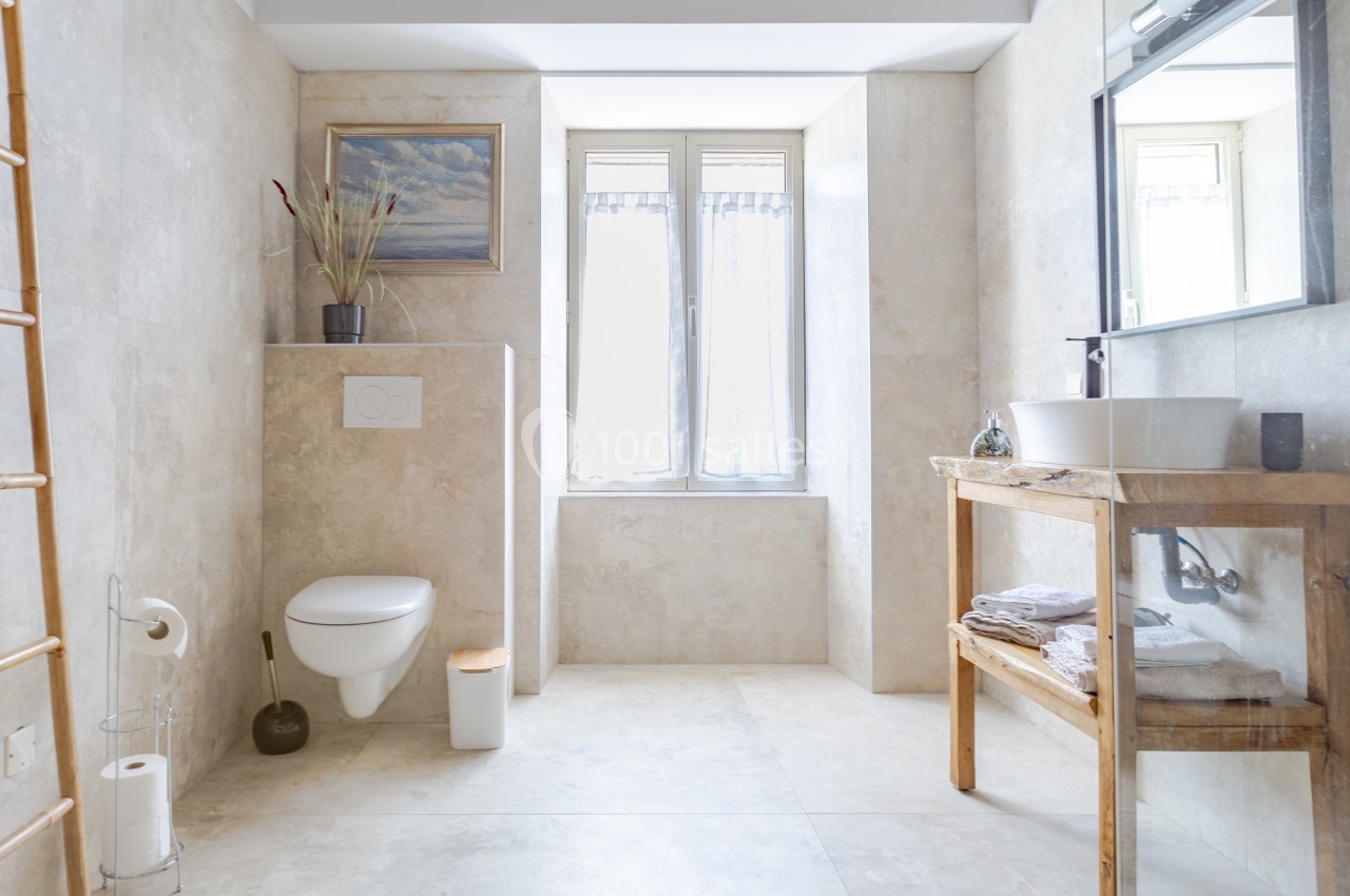 Salle de bain lumineuse avec toilettes suspendues, vasque sur meuble en bois et fenêtre laissant entrer la lumière naturelle.