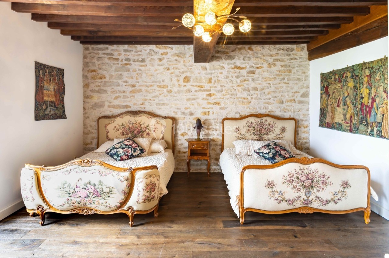 Deux lits anciens avec têtes et pieds décorés de motifs floraux, dans une chambre aux murs en pierre et poutres apparentes.