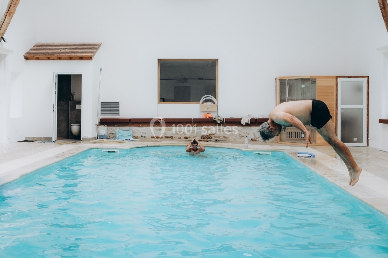 Un homme plonge dans une piscine intérieure tandis qu'une autre personne est assise dans l'eau.