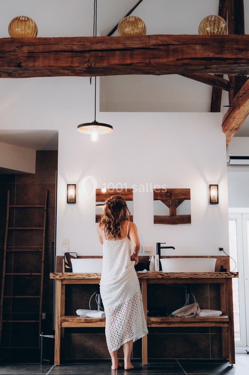 Femme de dos en robe légère, se tenant devant un lavabo double dans une salle de bain au style rustique.