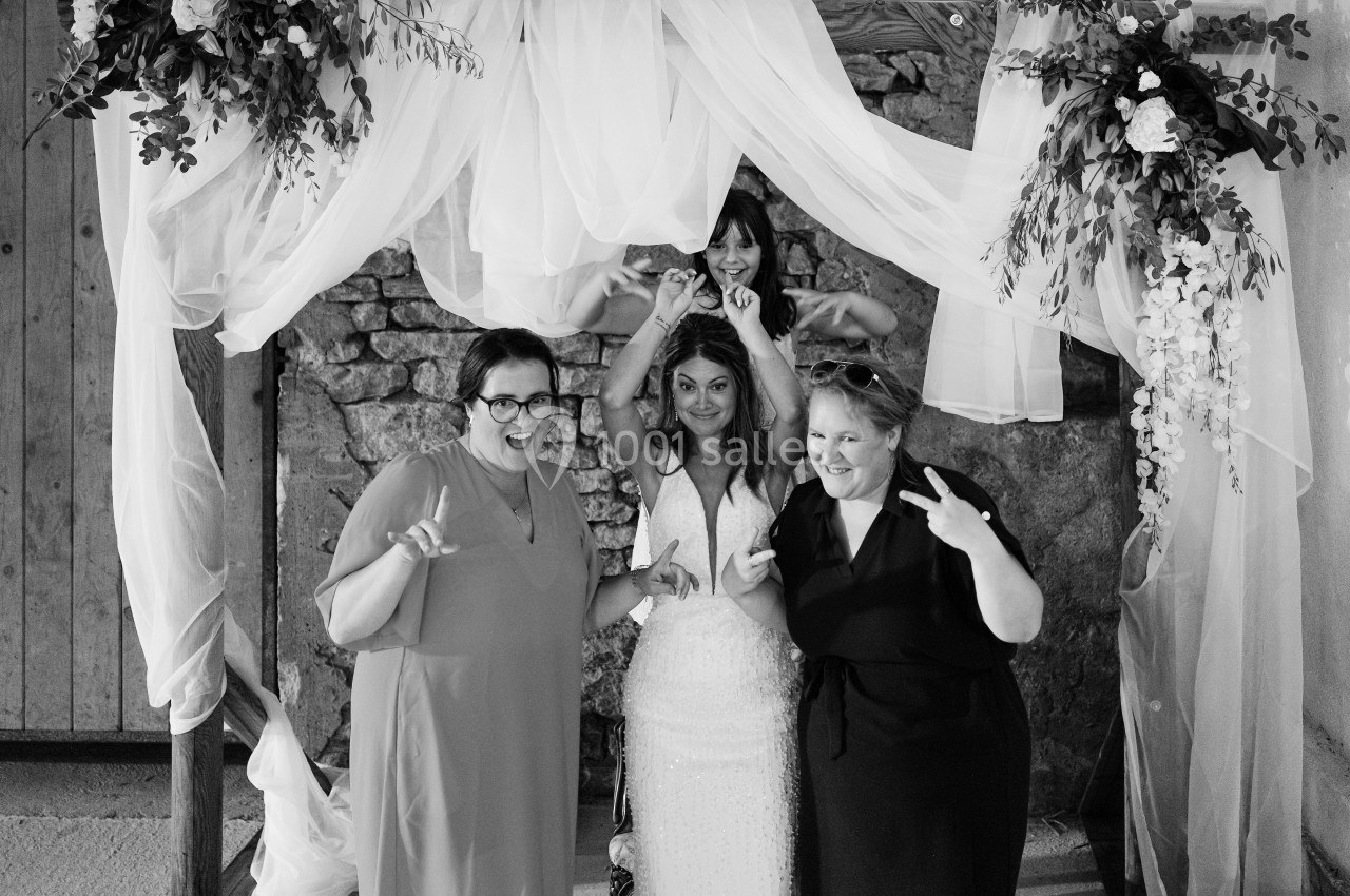 Quatre femmes souriantes posent sous une arche décorée de voilages et de fleurs lors d'un événement festif.