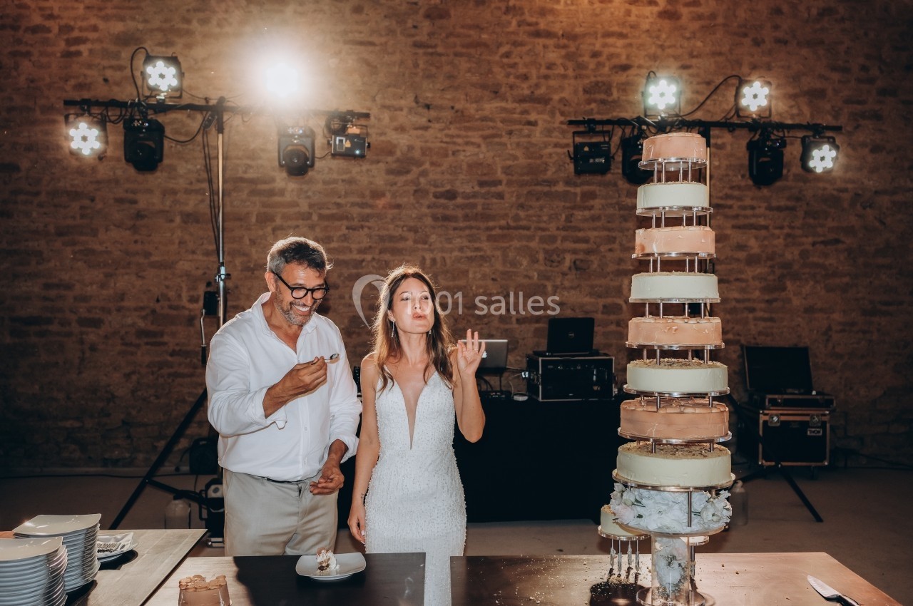 Un couple déguste un gâteau de mariage devant une pièce montée dans une salle en pierre éclairée.
