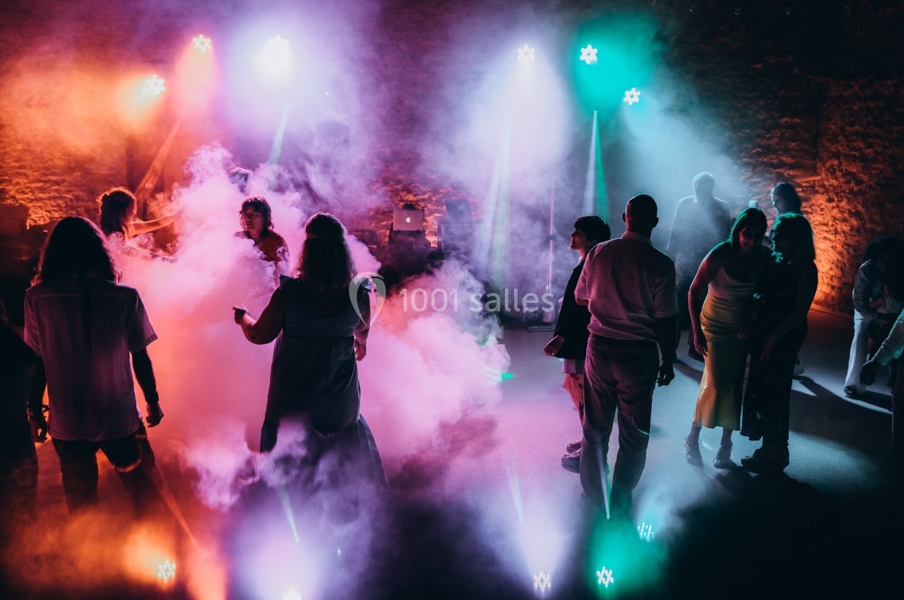 Personnes dansant dans une ambiance festive avec éclairages colorés et fumée sur une piste de danse.