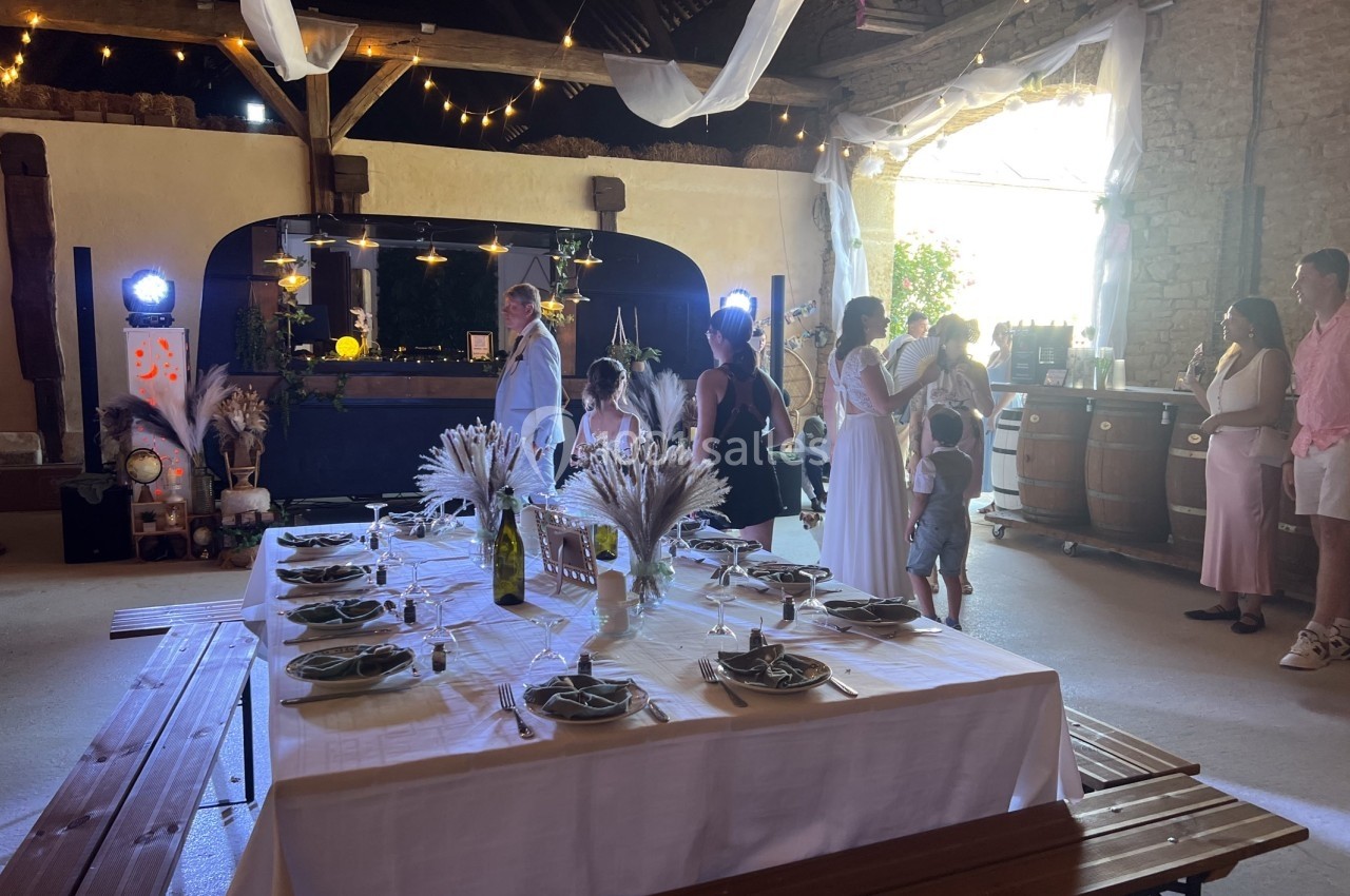 Salle de réception décorée pour un événement, avec une table dressée et des invités discutant près du bar.