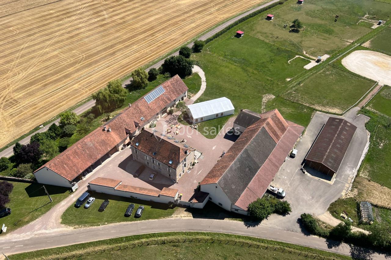 Vue aérienne d'un domaine rural avec bâtiments en U, cours centrale, champs et espaces verts environnants.