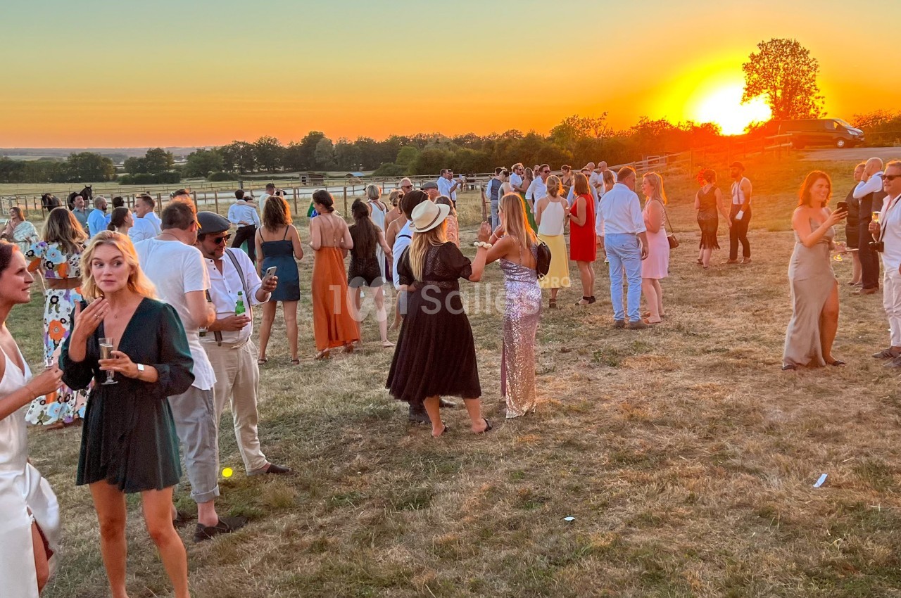 Groupe de personnes discutant en plein air lors d'un événement au coucher du soleil dans un cadre champêtre.