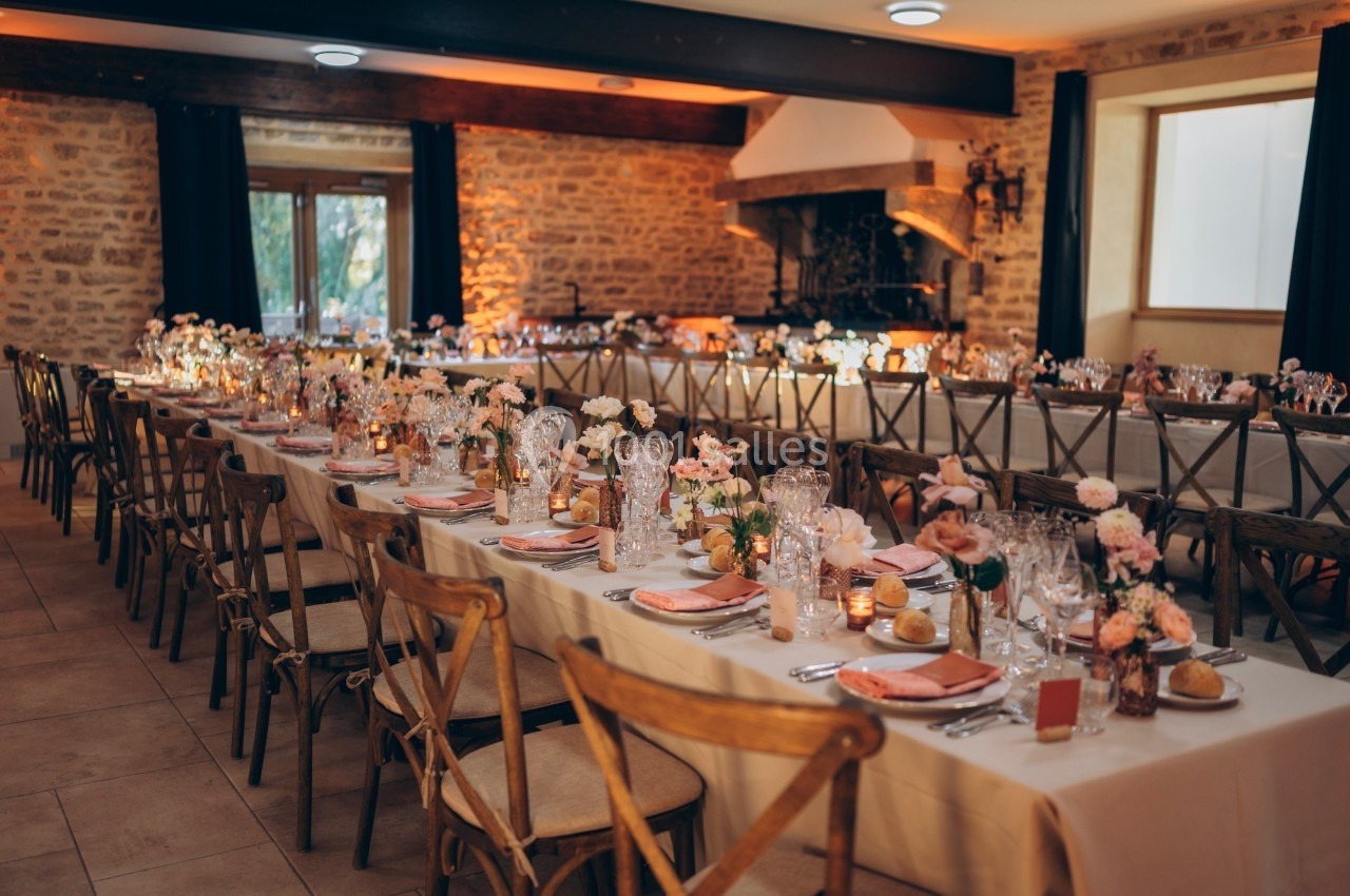 Salle de réception décorée pour un mariage, avec longues tables dressées, fleurs et lumière chaleureuse.