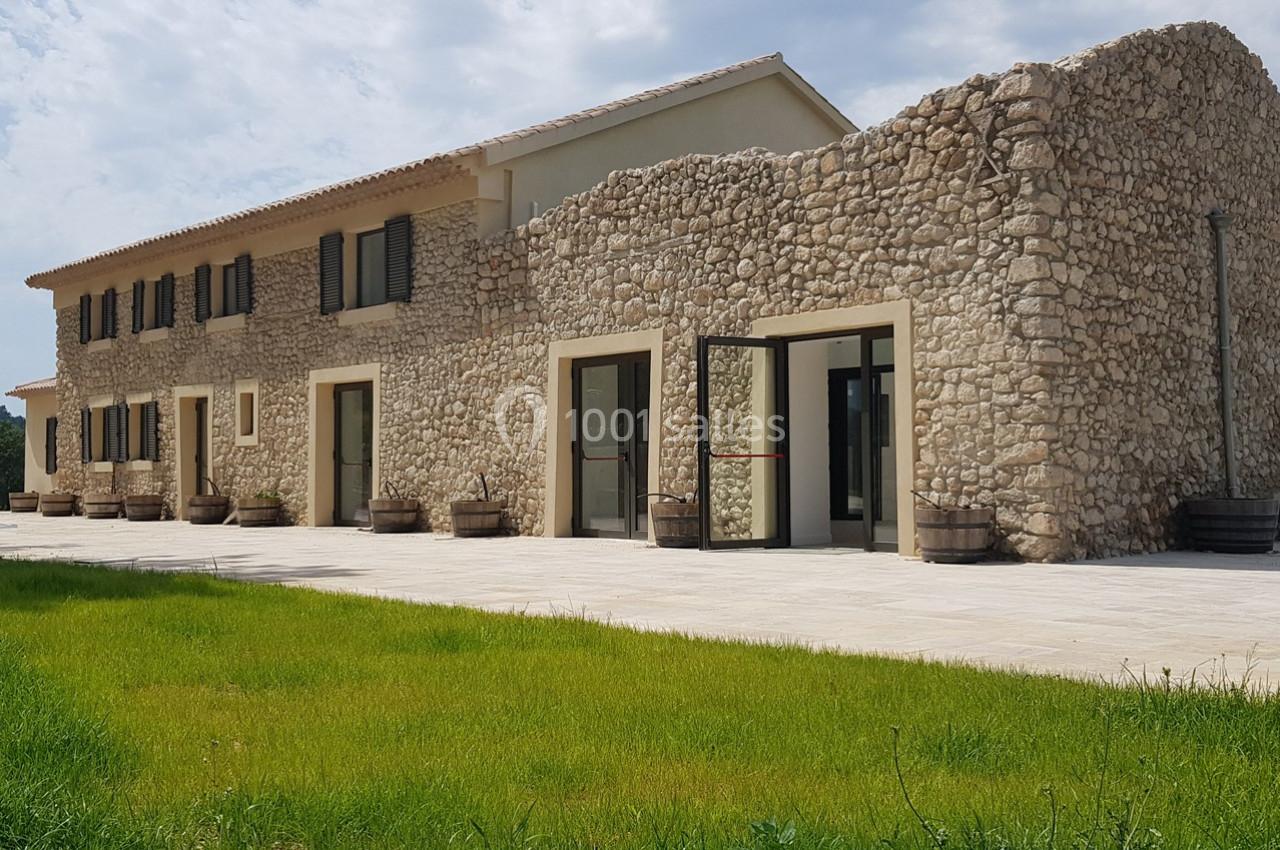 Bâtiment en pierre avec des fenêtres modernes, entouré d'une pelouse verte et d'un ciel partiellement nuageux.