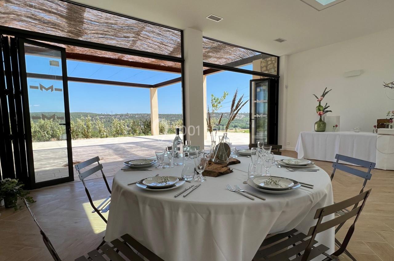 Table ronde dressée avec vaisselle élégante dans une salle lumineuse ouverte sur une terrasse avec vue panoramique.