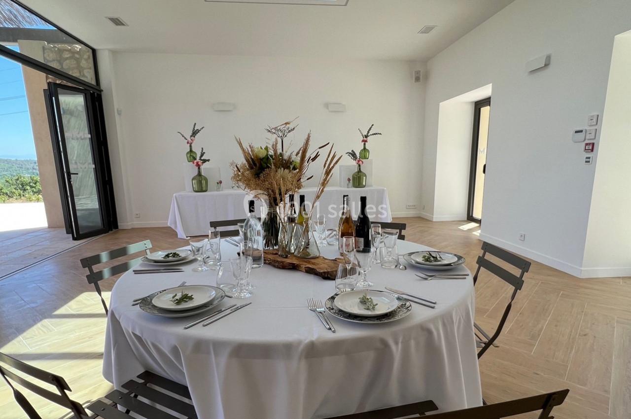 Table ronde dressée avec vaisselle élégante, centre de table floral, dans une salle lumineuse aux tons neutres.