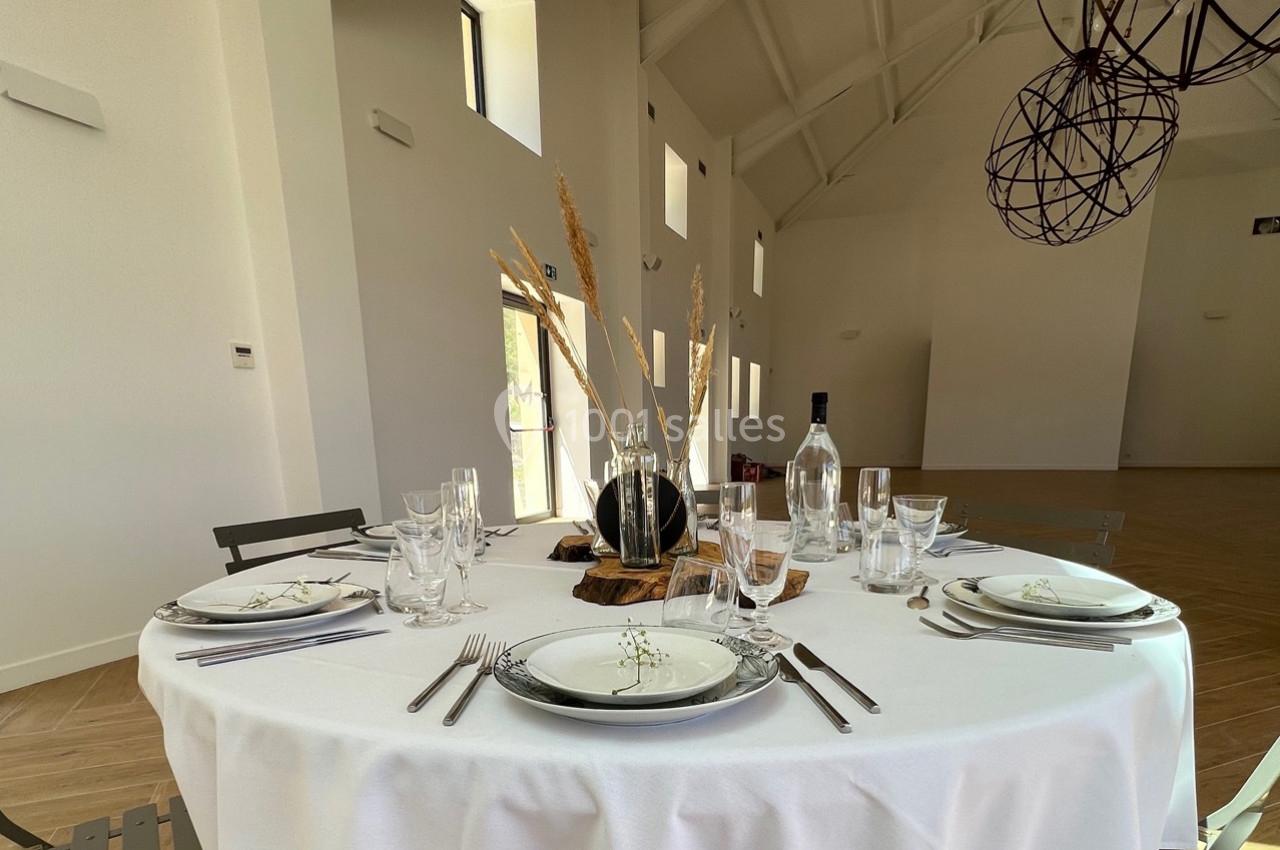 Table ronde dressée avec une nappe blanche, vaisselle élégante, décoration florale et bouteille d'eau dans une salle…