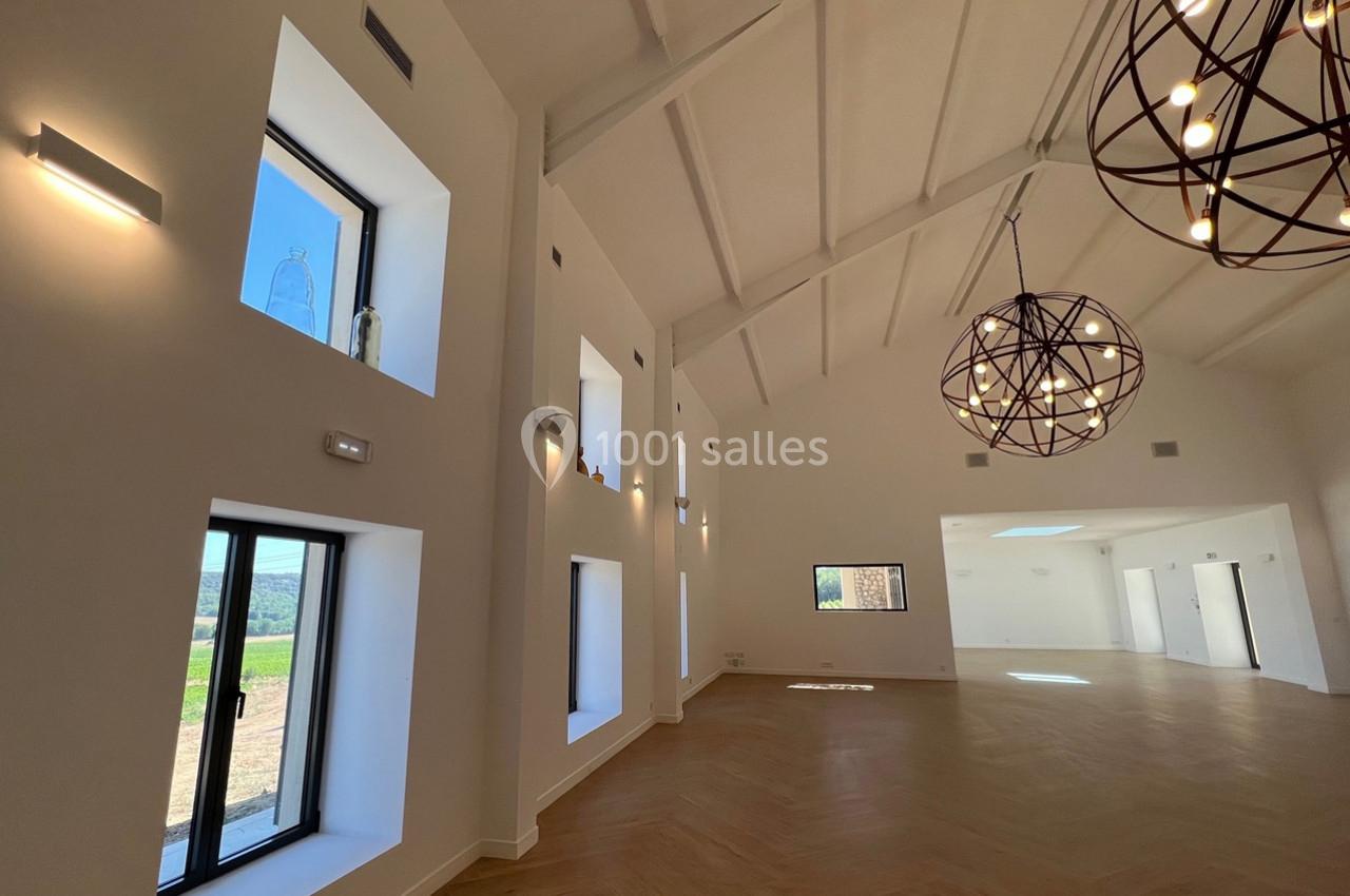 Salle lumineuse avec parquet en bois, grandes fenêtres, murs blancs et suspensions métalliques décoratives.