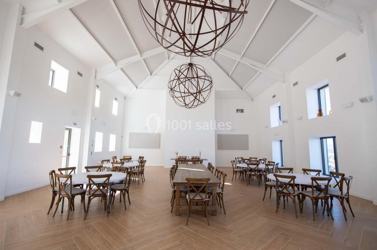 Salle lumineuse avec tables et chaises en bois, plafond haut et lustres sphériques suspendus.