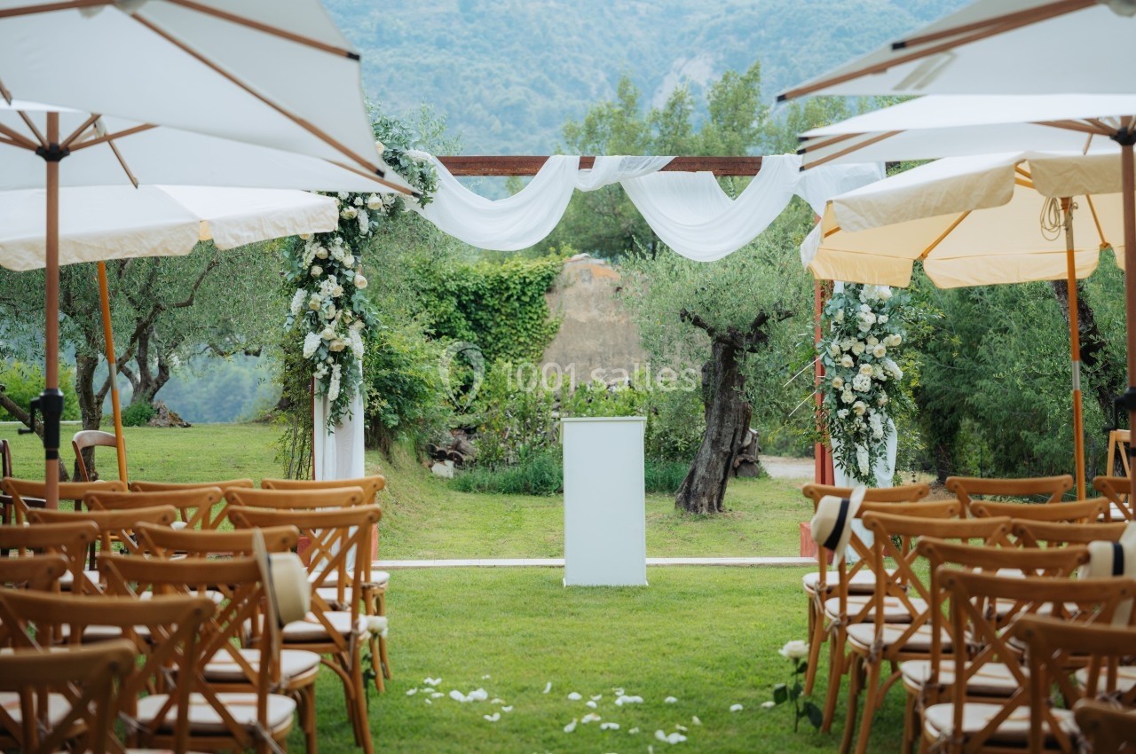 Allée centrale décorée pour une cérémonie en plein air, avec chaises en bois, fleurs blanches et vue sur un paysage…