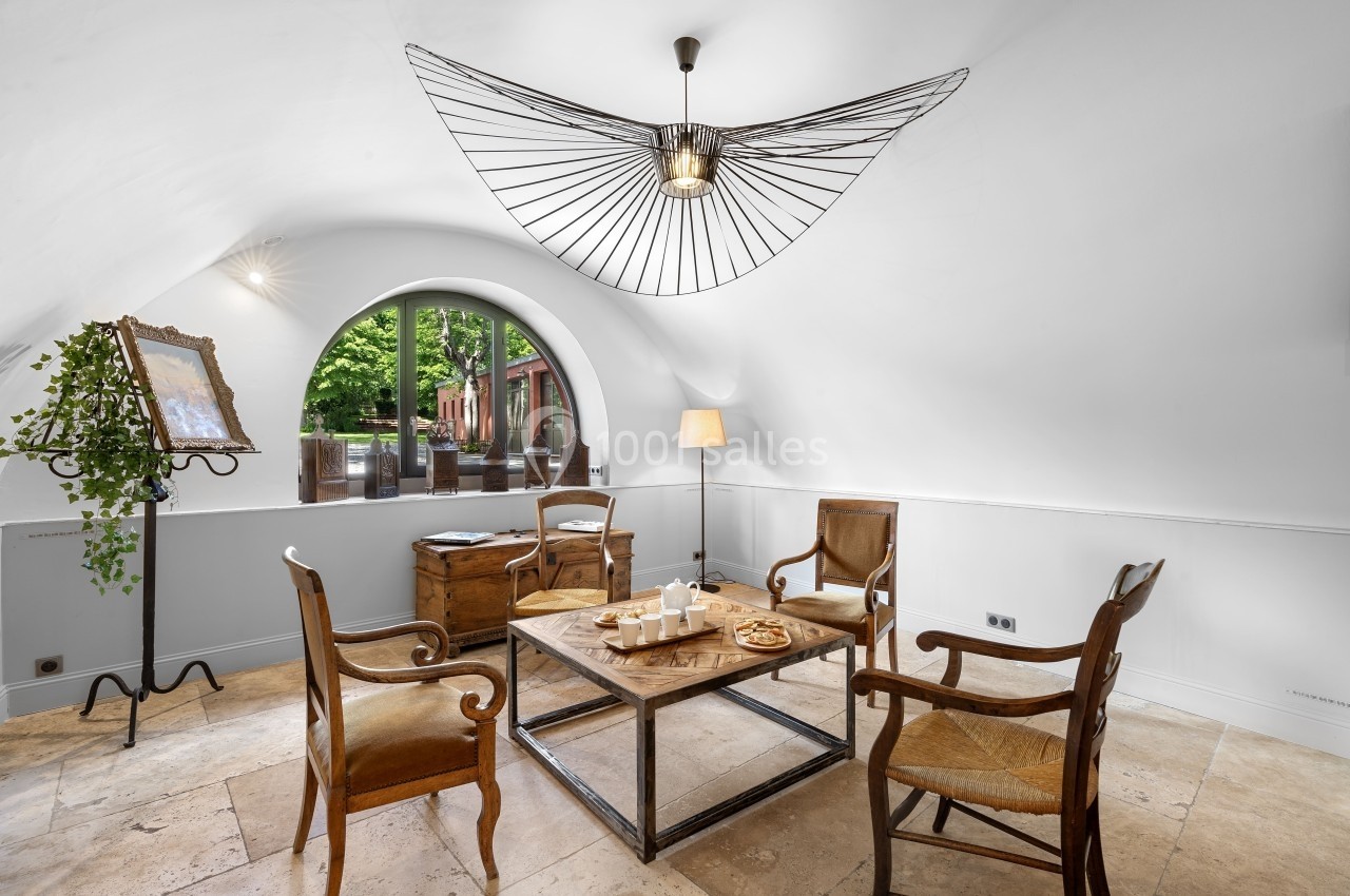 Salle lumineuse avec quatre chaises en bois autour d'une table basse, grande fenêtre cintrée et décoration minimaliste.