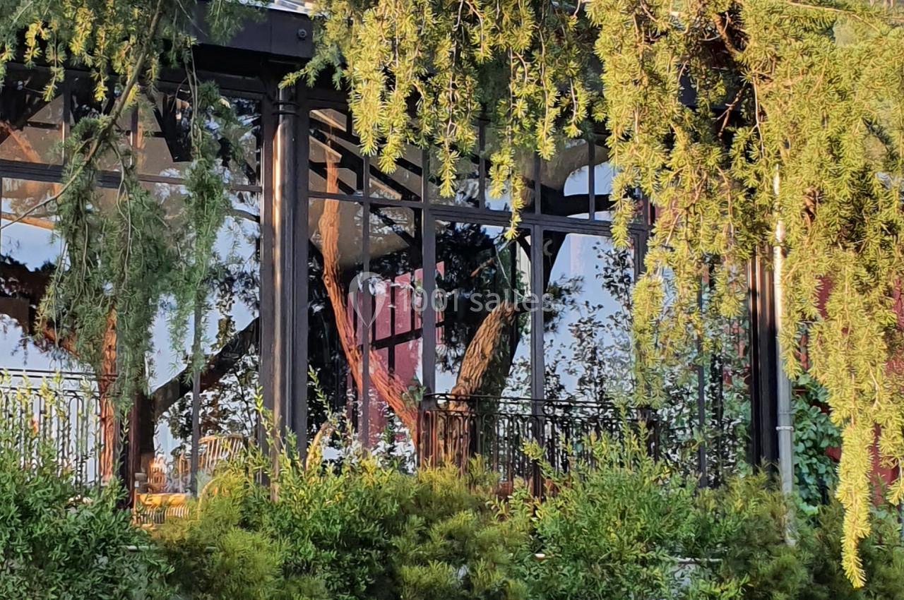 Façade d'un bâtiment entouré de végétation, avec des arbres et un banc en pierre au premier plan.