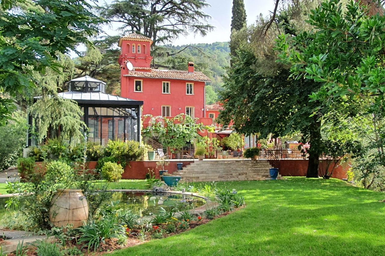 Grande maison rouge entourée de verdure, avec un jardin paysager, un bassin et des arbres matures.