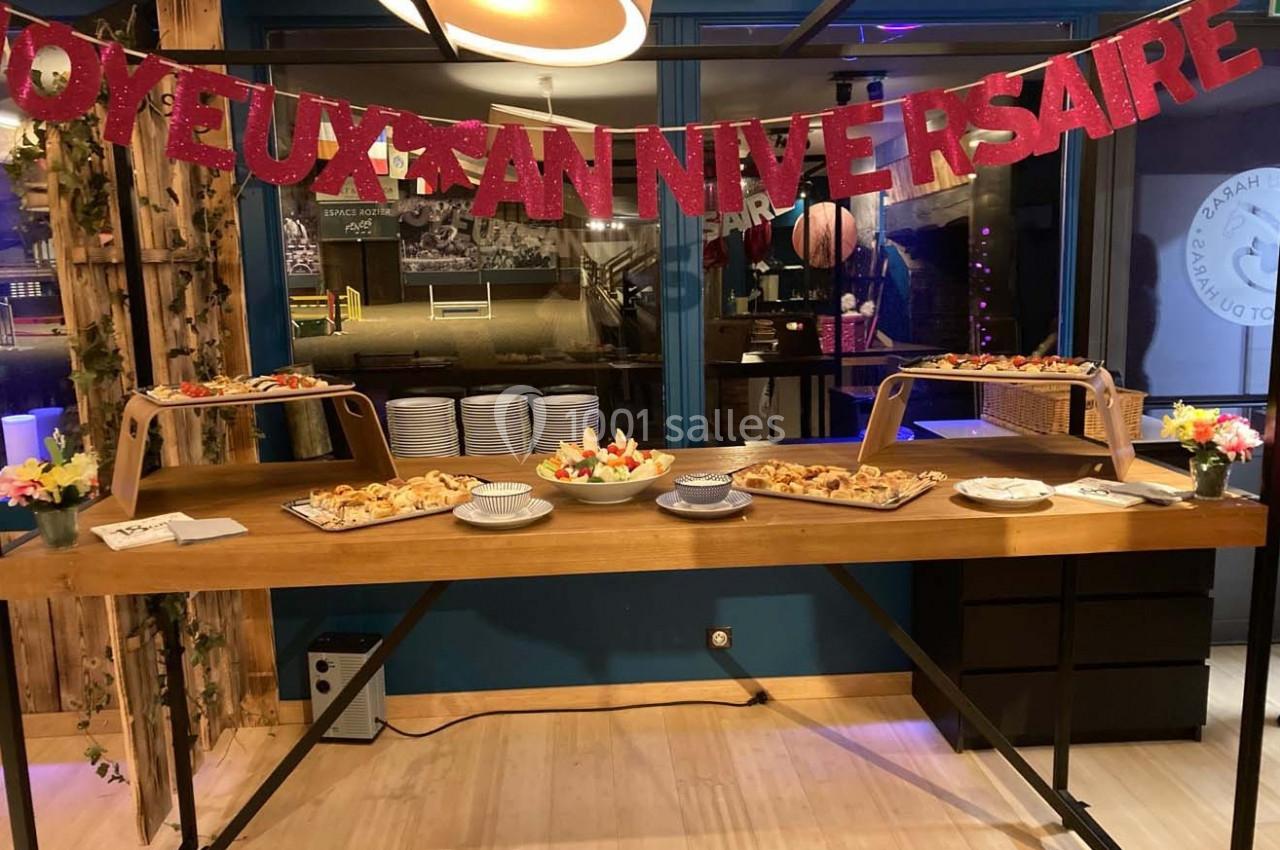 Buffet d'anniversaire avec des plats variés, décoré d'une guirlande rouge ’Joyeux Anniversaire’ dans une salle lumineuse.