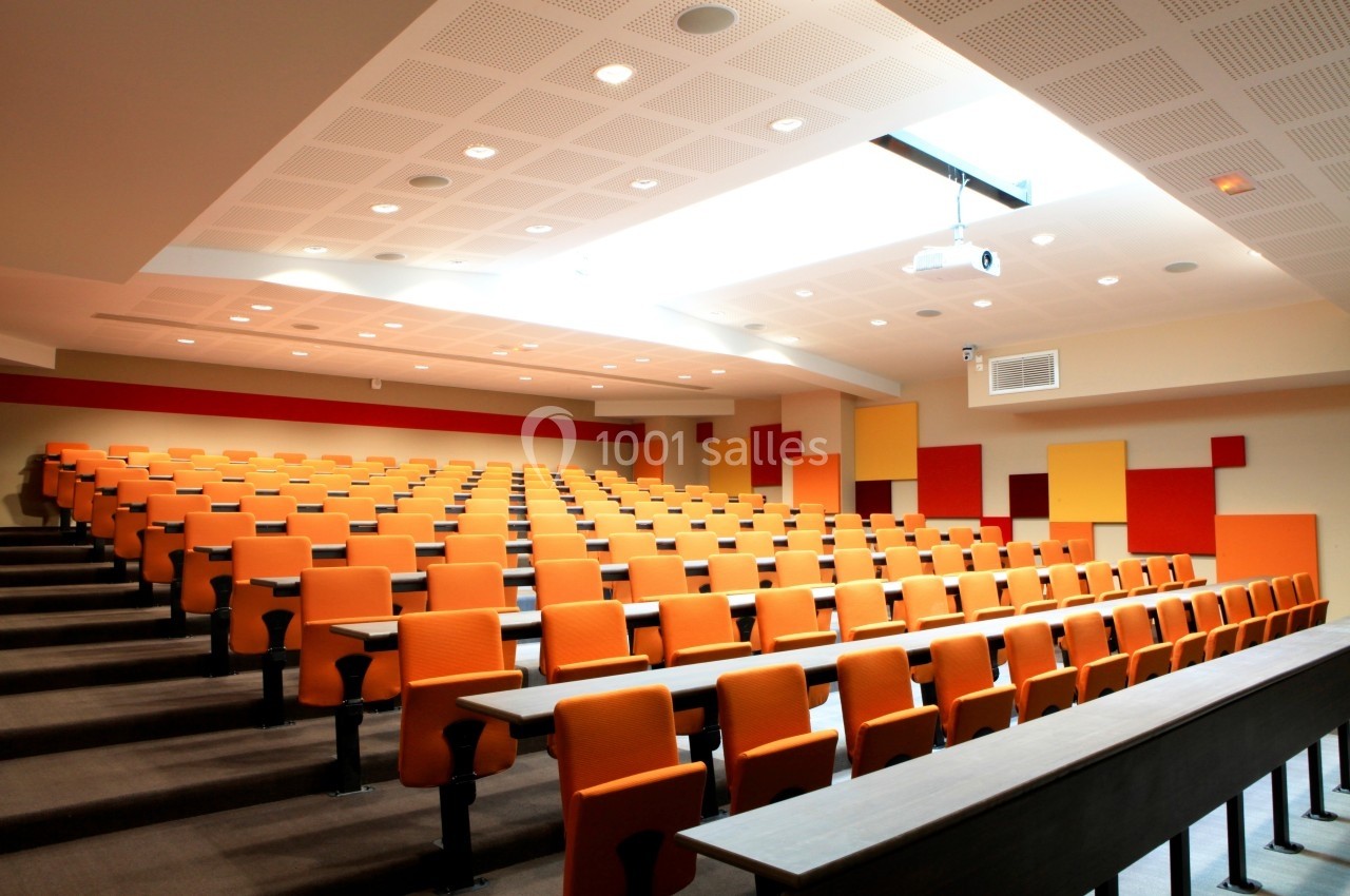Salle de conférence moderne avec des rangées de sièges orange et un projecteur suspendu au plafond.