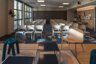 Salle de conférence moderne avec des rangées de sièges orange et un projecteur suspendu au plafond.