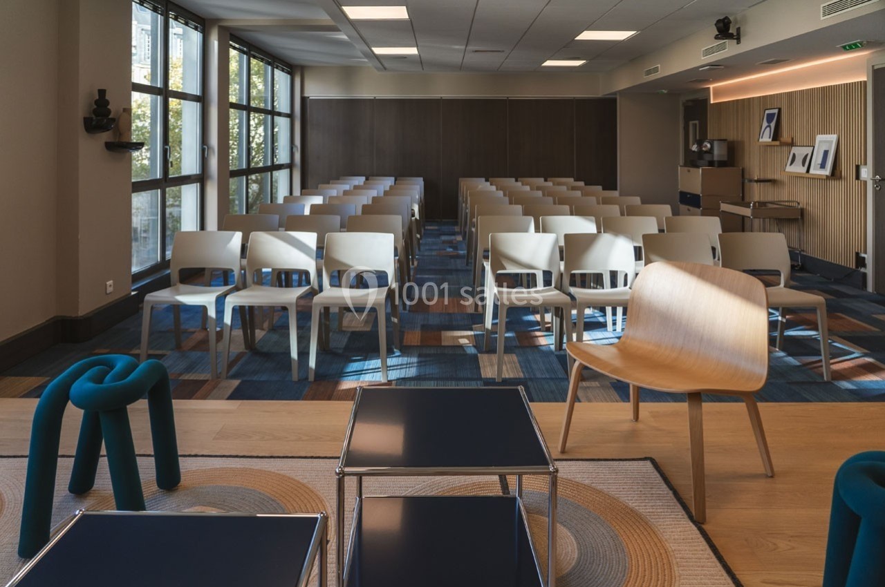 Salle de conférence lumineuse avec rangées de chaises alignées, grandes fenêtres et décor moderne.