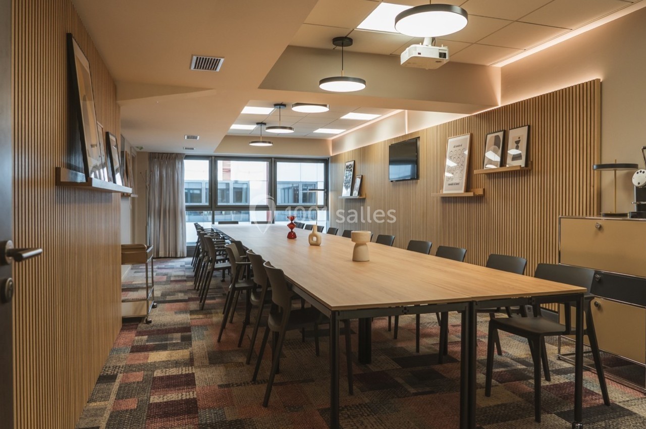 Salle de réunion moderne avec une grande table en bois, des chaises noires et un éclairage chaleureux.