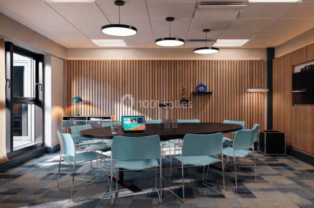 Salle de réunion moderne avec table ronde, chaises bleues, éclairage suspendu et mur en bois lamellé.