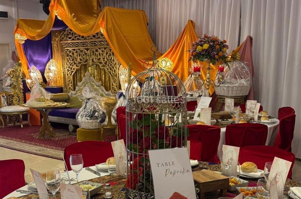 Décoration de salle de réception avec table dressée, cage décorative, trône doré et drapés colorés en arrière-plan.
