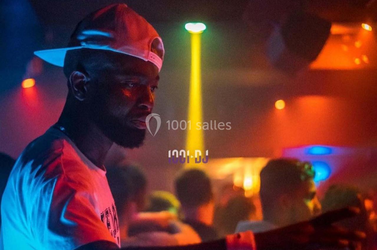 Un DJ portant une casquette blanche mixe dans une ambiance de boîte de nuit colorée et éclairée par des lumières vives.