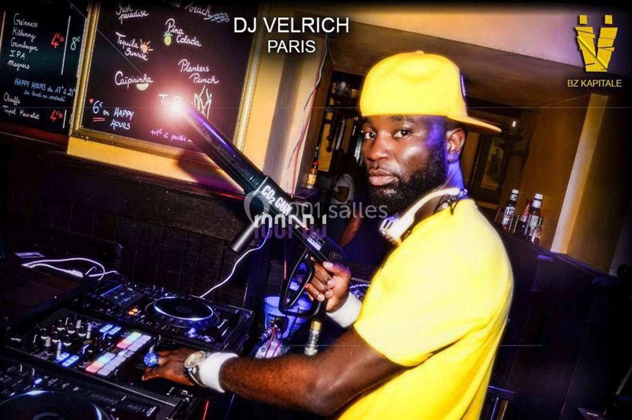 Un DJ portant une casquette jaune mixe de la musique dans un club, entouré d'équipements audio et de lumières colorées.