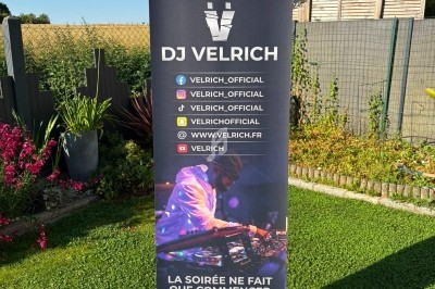 Un DJ en tenue originale mixe en extérieur devant une foule assise à des tables de café en terrasse.