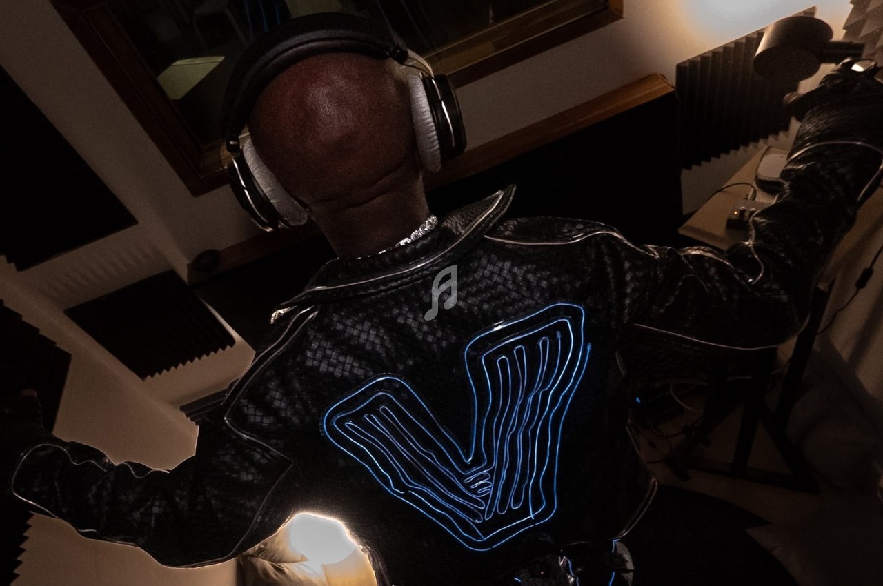 Personne de dos portant un casque audio et une veste avec un motif lumineux, dans un studio d'enregistrement.