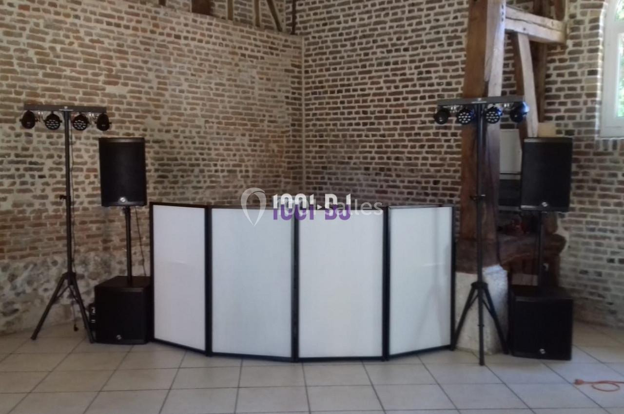 Console de DJ avec éclairage et enceintes, installée dans une salle en briques avec une fenêtre à droite.